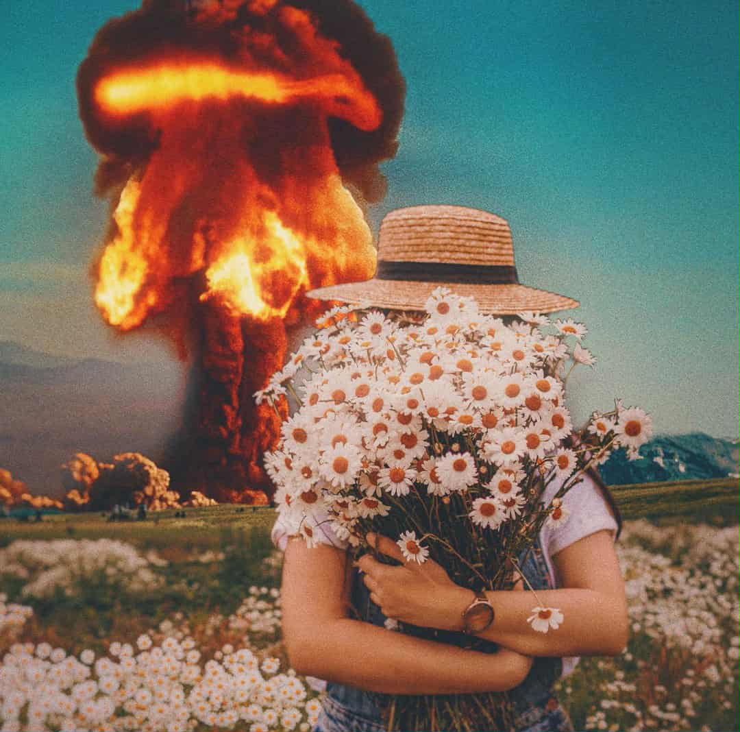A person in overalls and a straw hat holds a large bouquet of daisies, standing in a field. A large explosion with fiery clouds looms in the background.